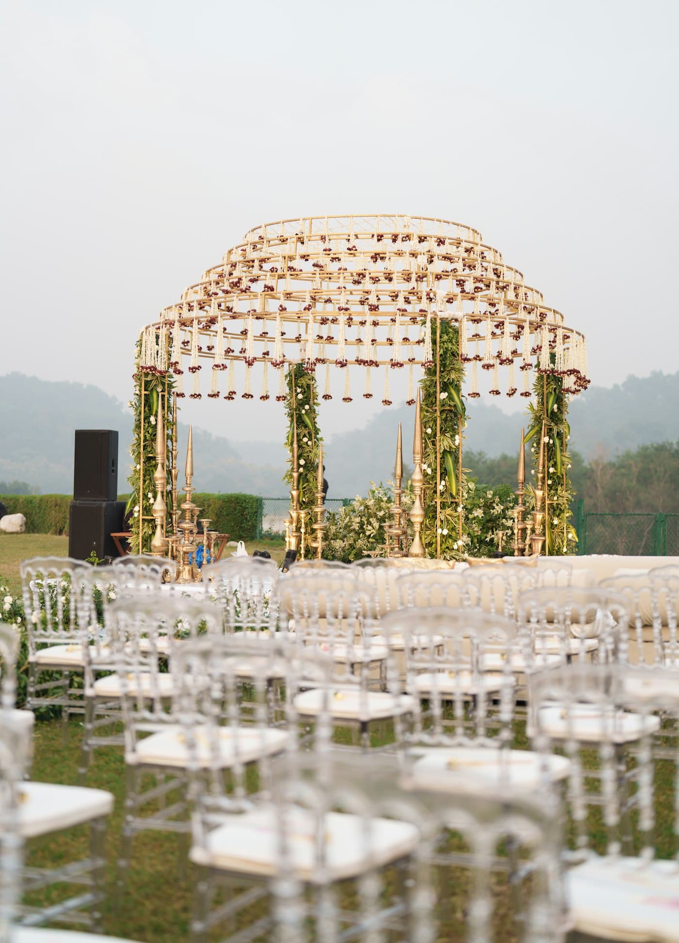 An outdoor ceremony setup on a lawn with draped floral structure and rows of seating
