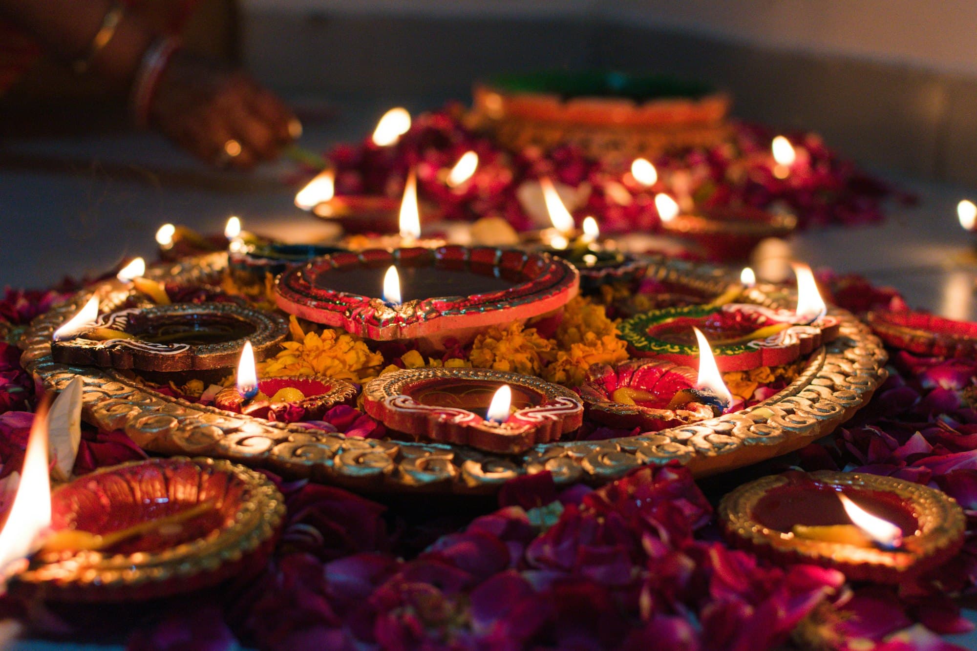 Lit clay oil lamps on a decorated tray with scattered petals