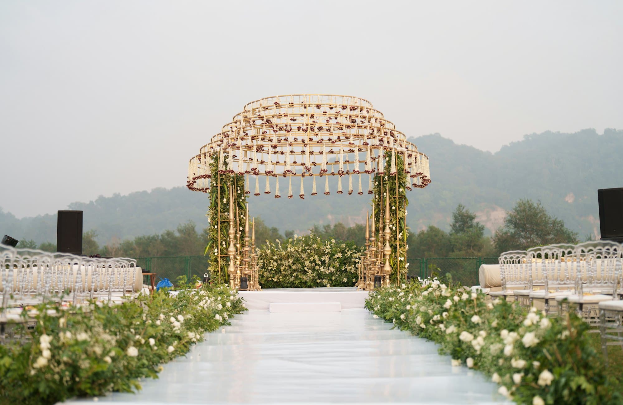 A floral wedding arch at the end of a flower-lined aisle on a green lawn
