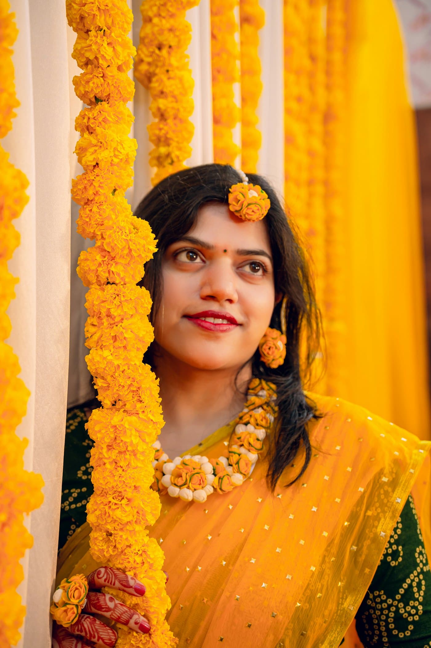 A smiling woman in a yellow sari holding a marigold garland
