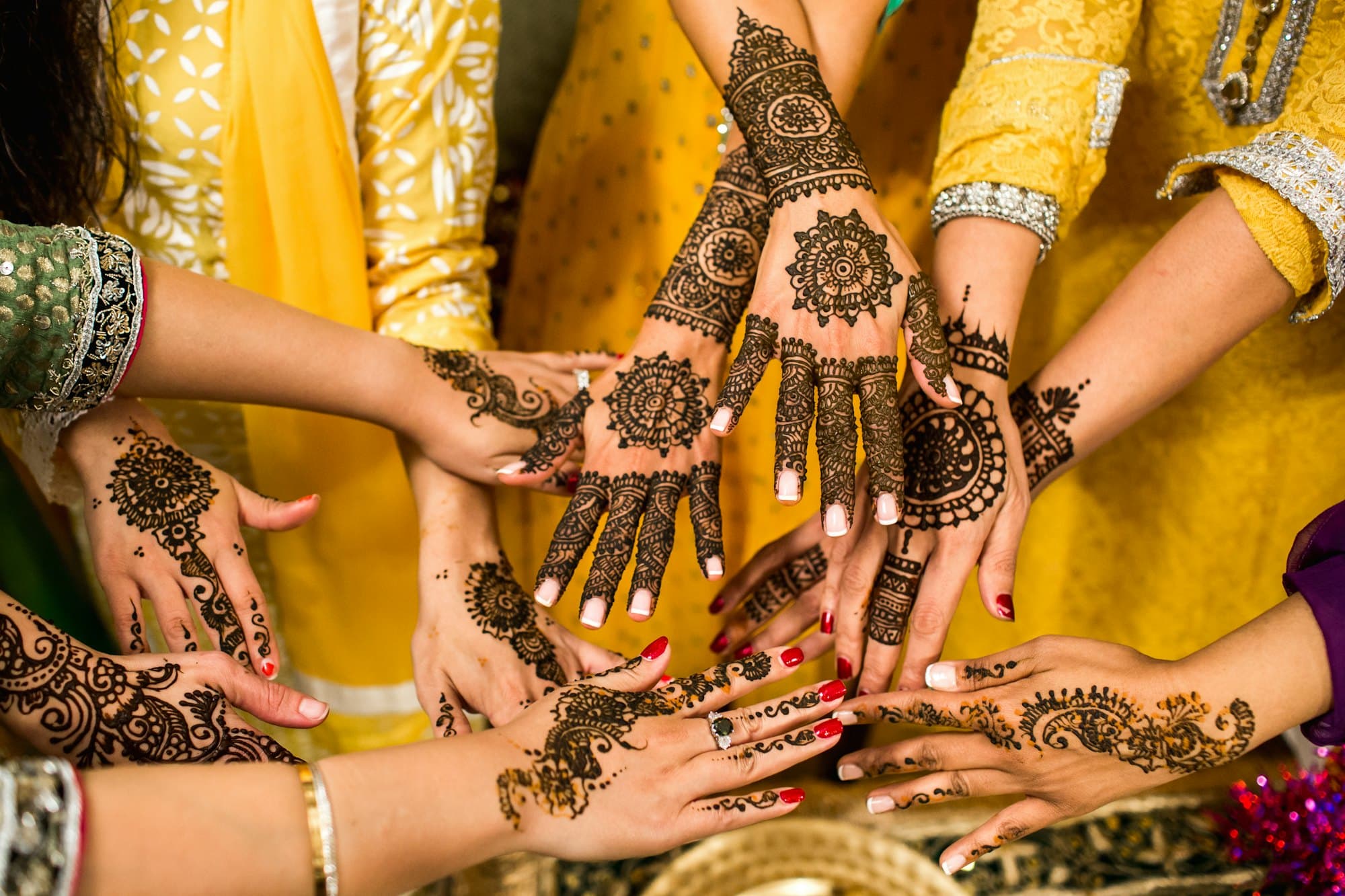 Several hands held together, decorated with intricate henna patterns